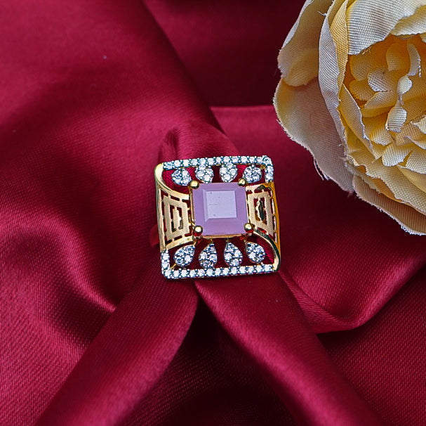 square-shaped gold ring featuring a pink gemstone in middle and diamonds.