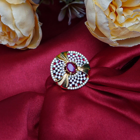 Round shaped gold ring with red gemstone in middle and dimonds.
